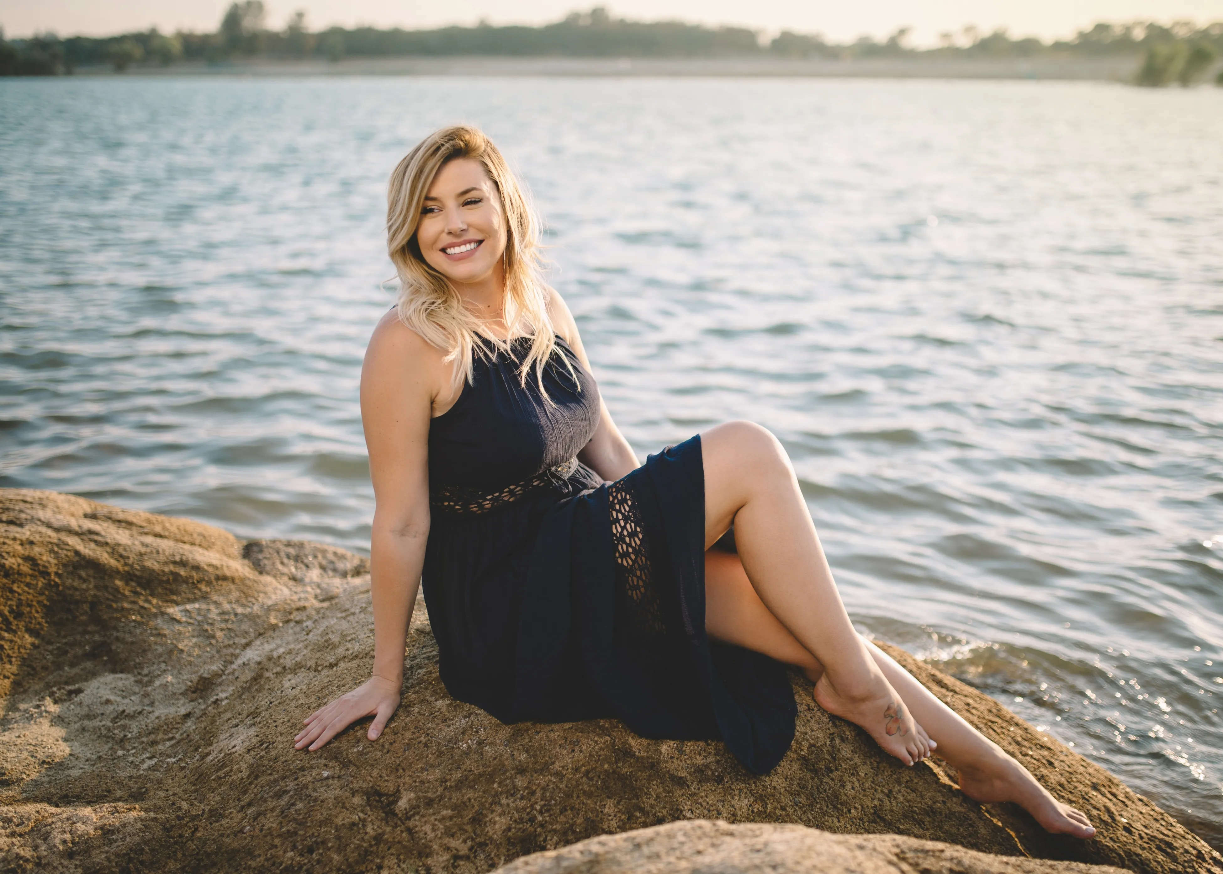 A woman smiling, sitting on a rock by the beach