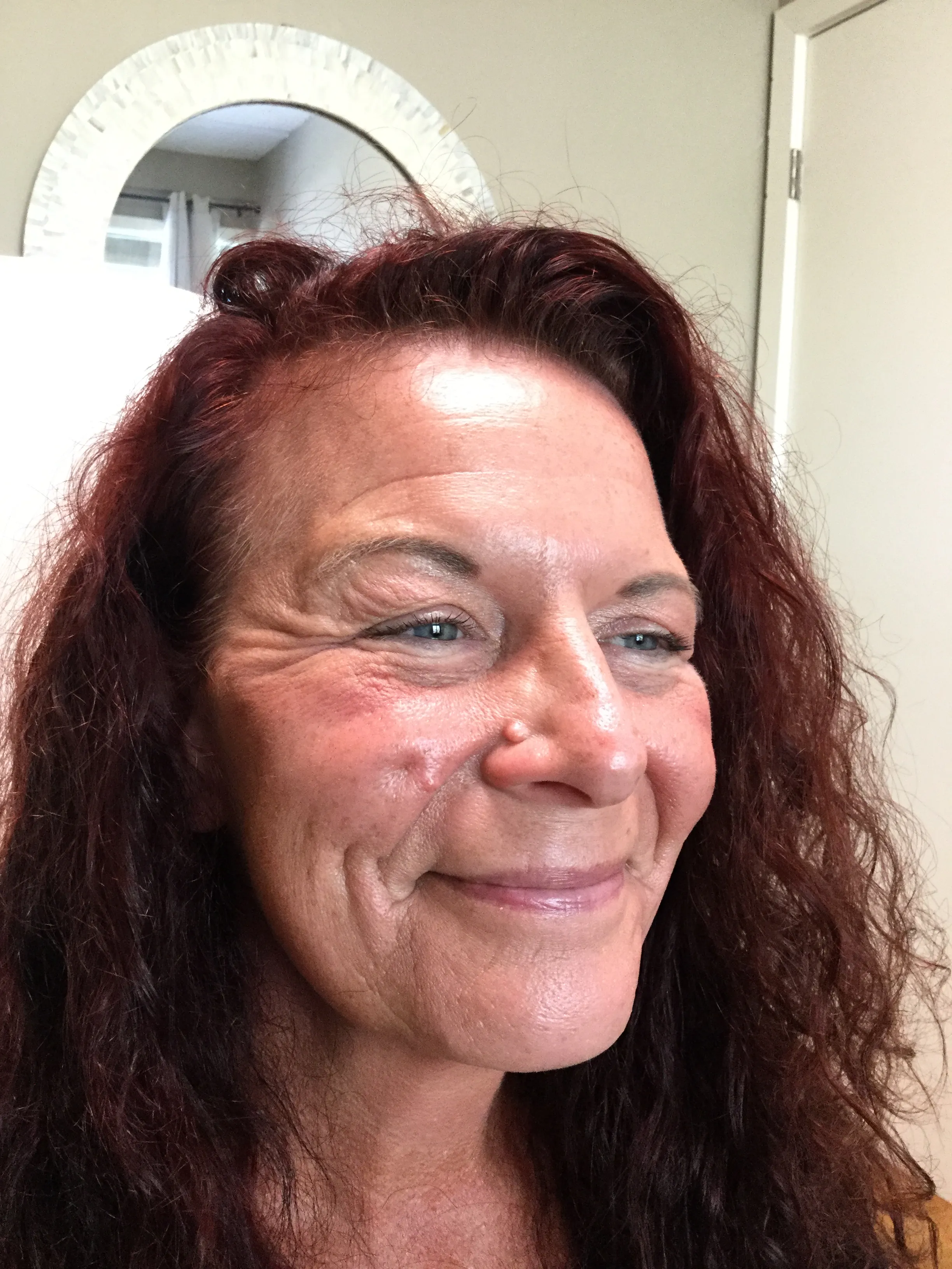 Smiling middle-aged woman with red curly hair, visible wrinkles around her eyes and cheeks.