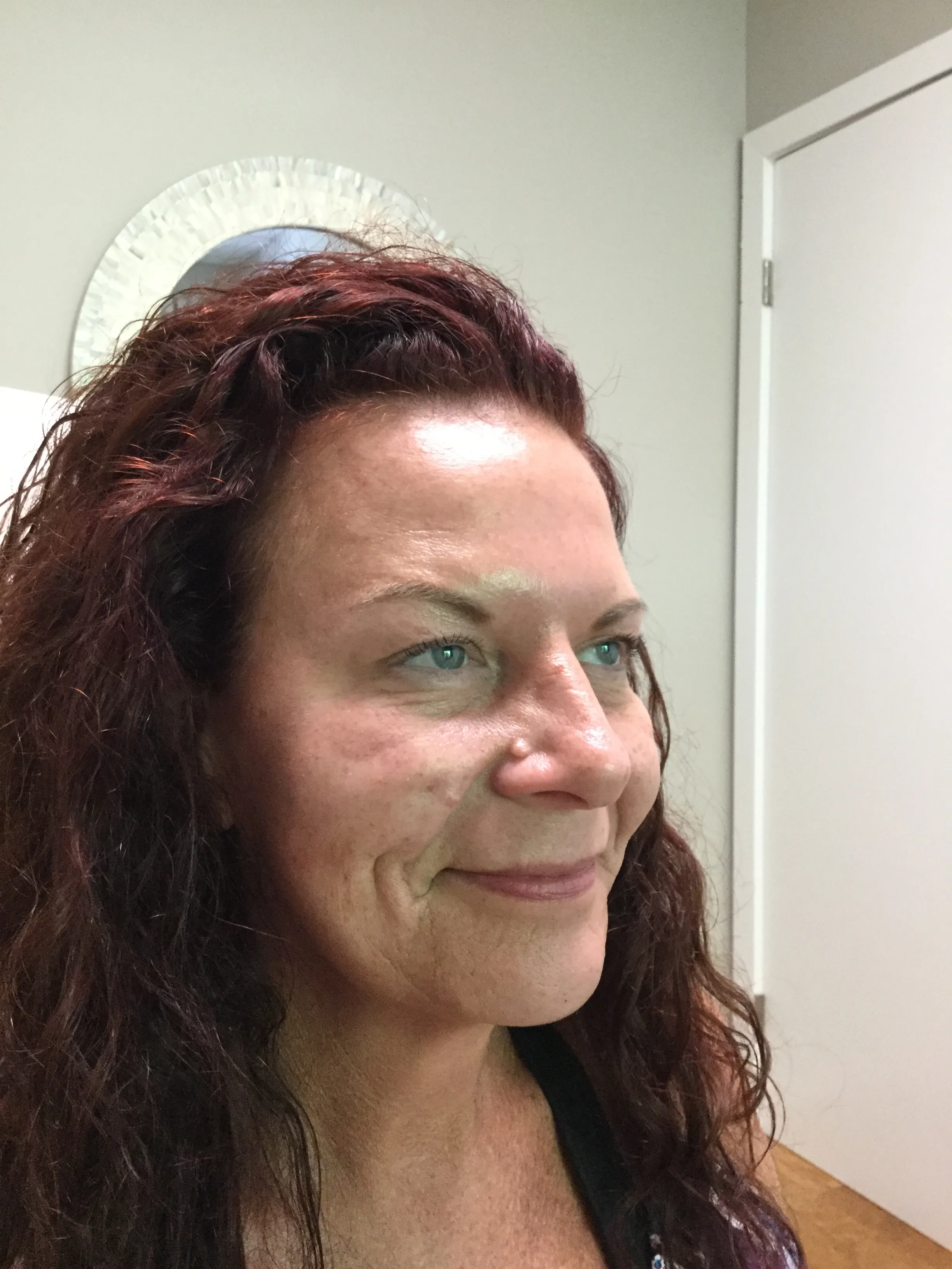 Side profile of a woman with curly red hair, blue eyes, and clear skin smiling softly indoors.