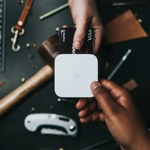 Hands holding a white Square card reader with a black Visa credit card being swiped through it.