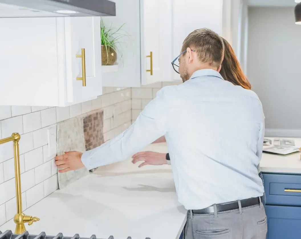 Man and woman examining tile samples against a kitchen backsplash in a modern kitchen.