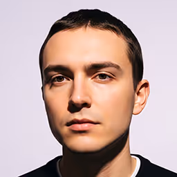 Close-up portrait of a young man with short dark hair and a neutral expression against a light background.