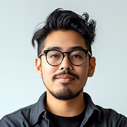 Headshot of a young man with black hair, glasses, and a goatee wearing a dark button-up shirt.