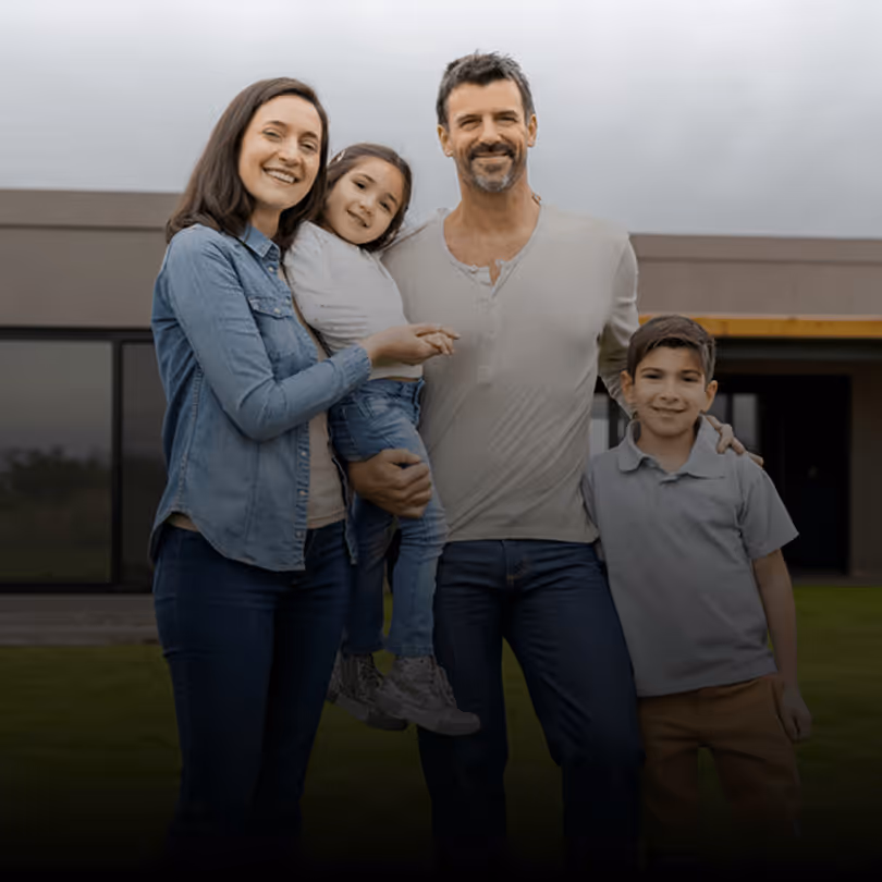 Eine glückliche Familie mit zwei Kindern steht draußen vor einem modernen Gebäude und lächelt in die Kamera.