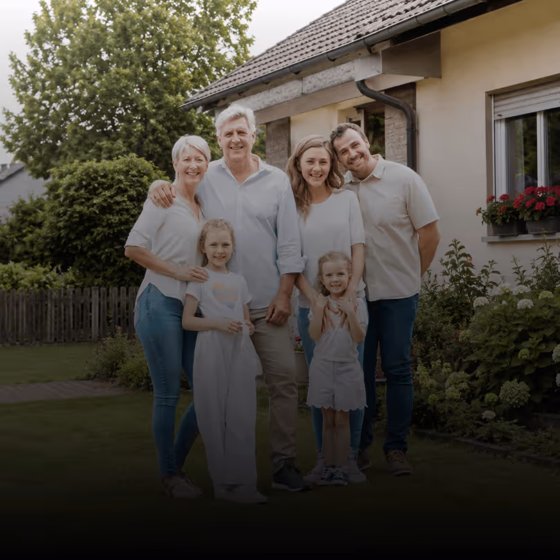 Familie lächelt vor modernem, weißem Haus mit Garten und Veranda.