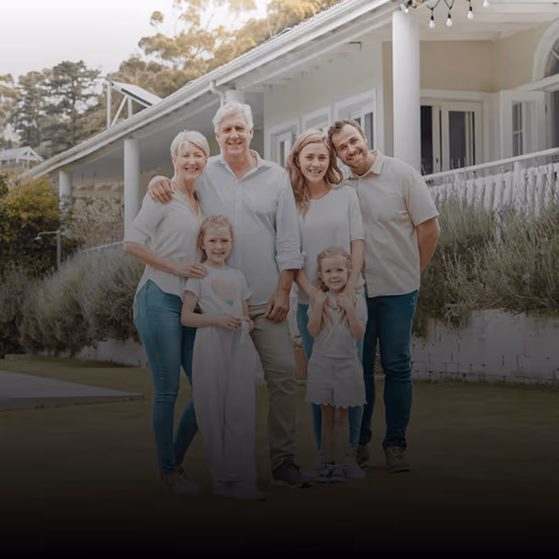 Familie lächelt vor modernem, weißem Haus mit Garten und Veranda.