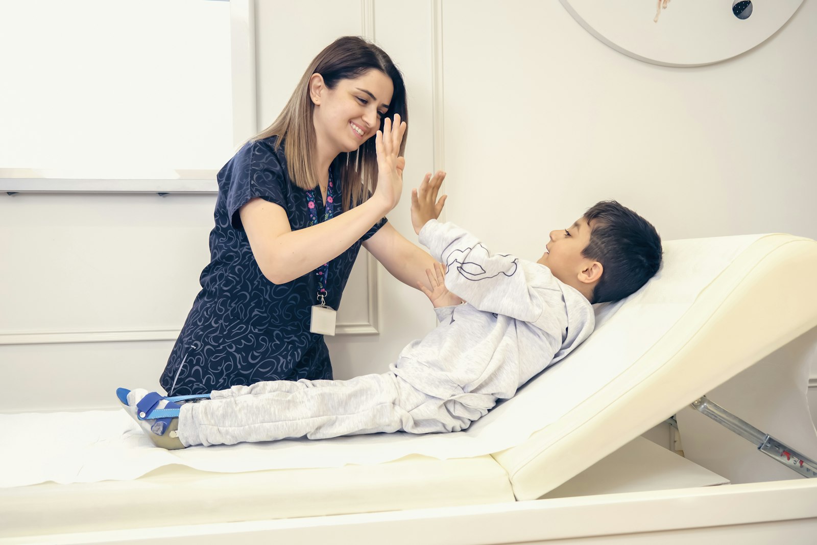 A therapist gives a high five to a smiling boy lying on a therapy table.