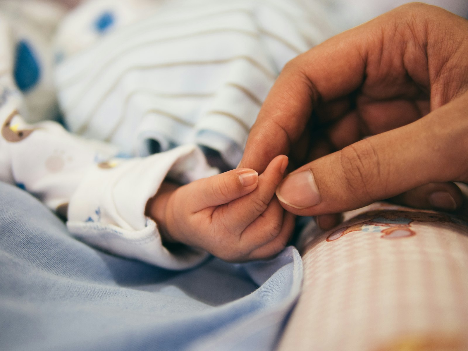 A newborn baby's hand holding an adult's finger.