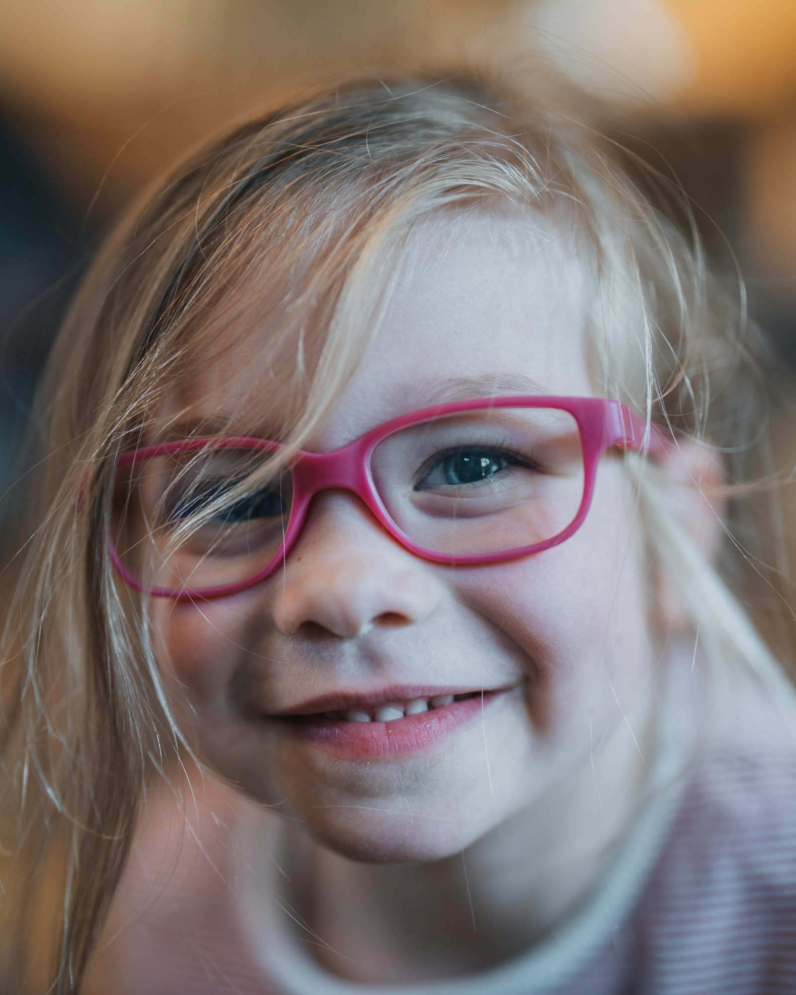 Close-up of a smiling young girl wearing pink-framed glasses.