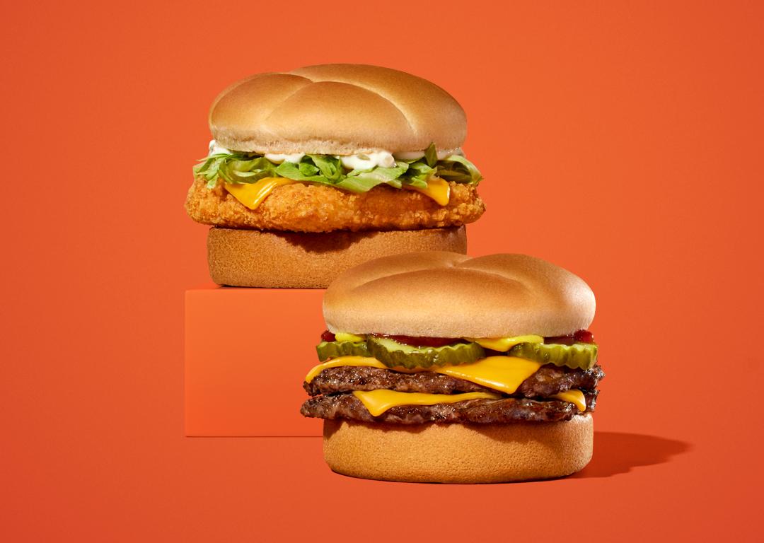 Two cheeseburgers on orange background; one has fried chicken, lettuce, and mayo, the other has double beef and pickles.