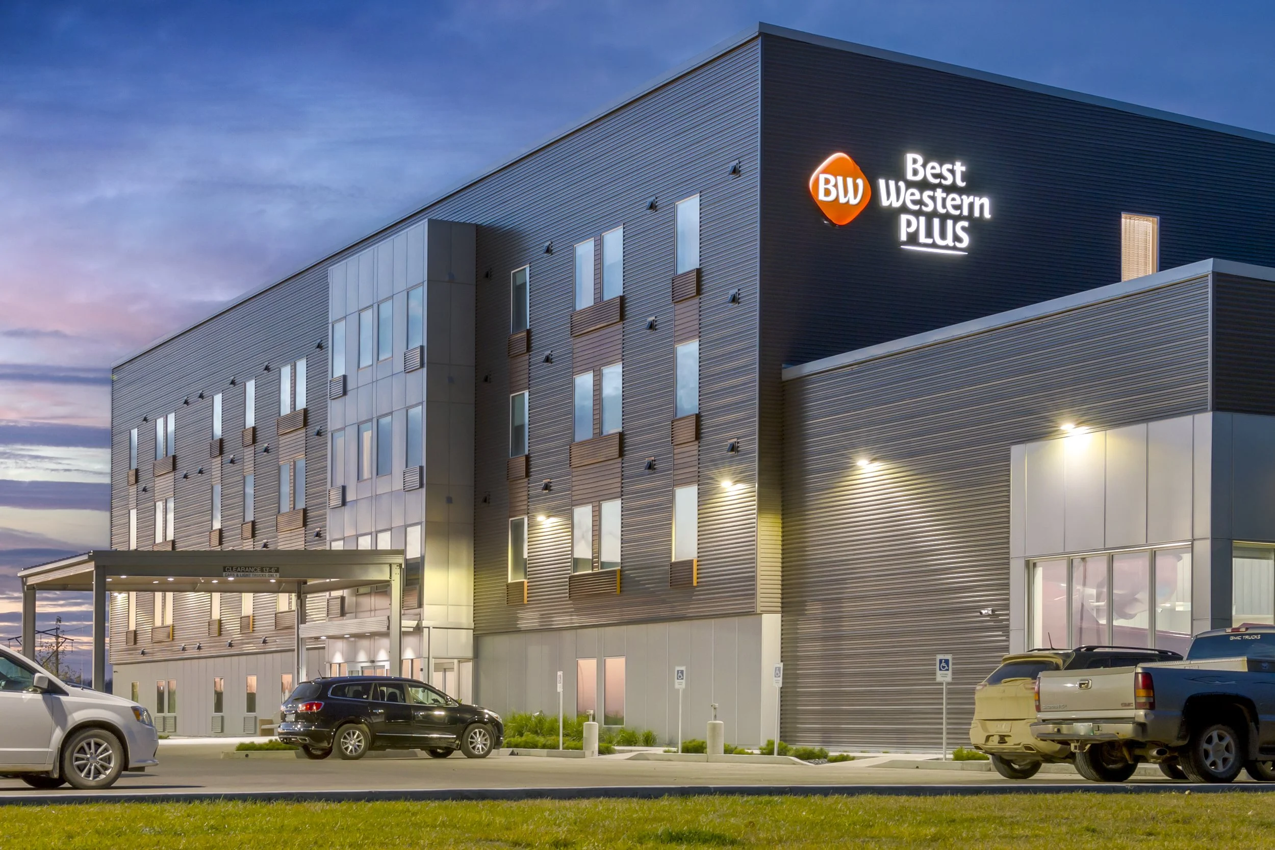 Exterior of Best Western Plus hotel at dusk with parked cars in front of the building.