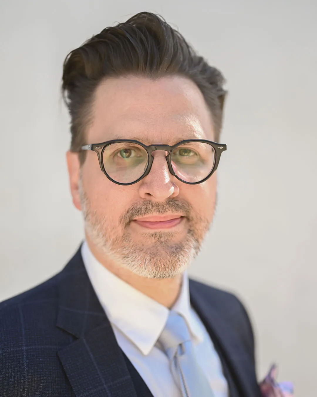 Mann mit Brille, leichtem Bart und Anzug vor weißem Hintergrund