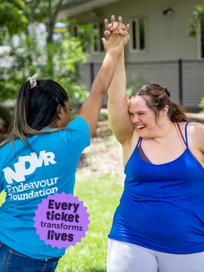 Two women outdoors smiling and holding hands raised together in a gesture of celebration.