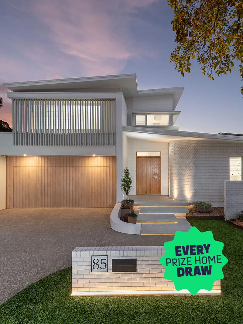Modern two-story house at dusk with a wooden garage door, illuminated steps, curved white brick wall, and house number 85.