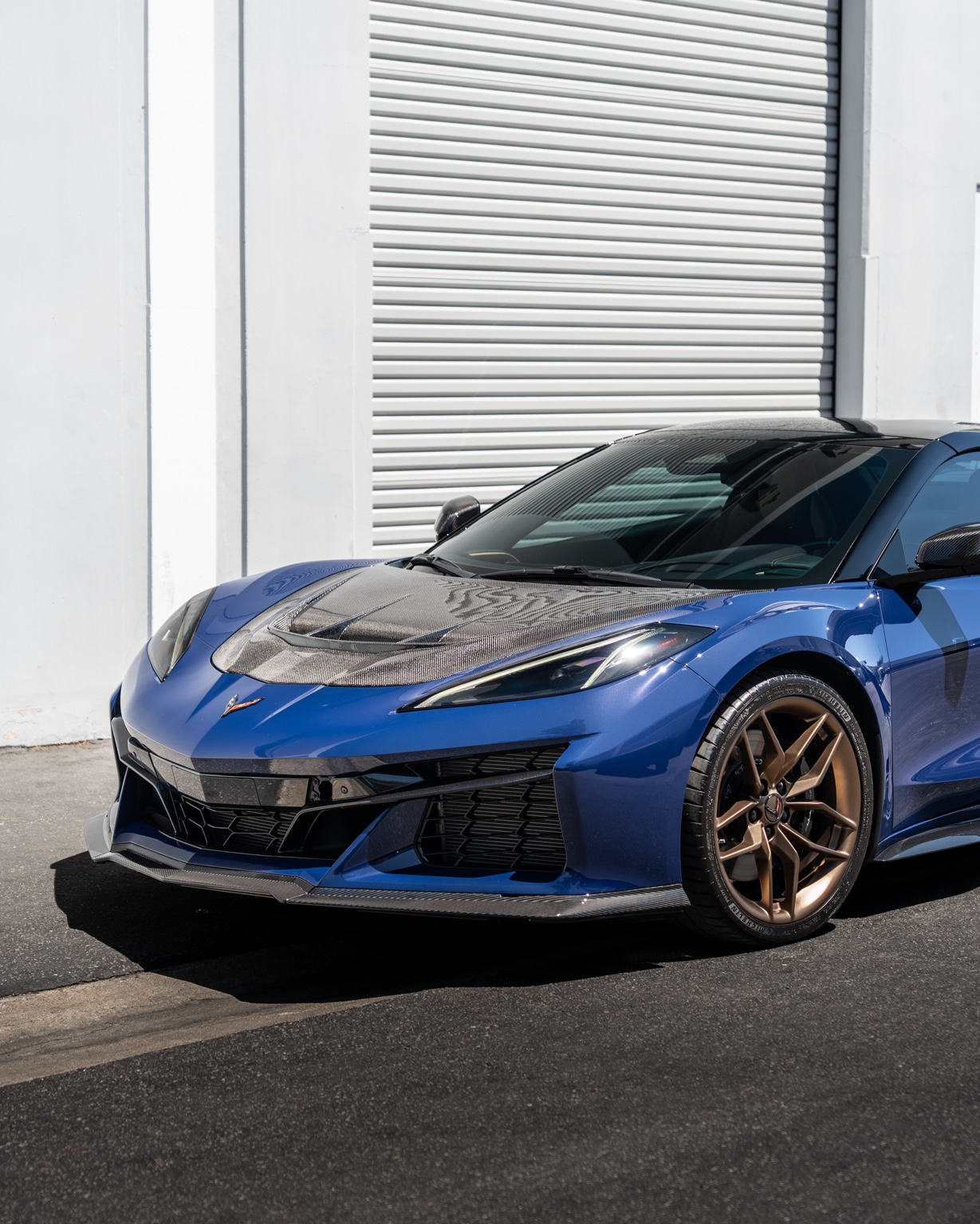 Blue Corvette C8 Z06 with a carbon hood and bronze wheels, front three quarter view, the $595 a day car in a guide to what it costs to rent a Corvette