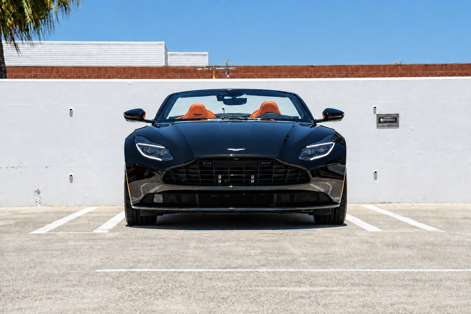 Head-on view of the black Aston Martin DB11 Volante with the roof down, orange leather seats showing over the windscreen