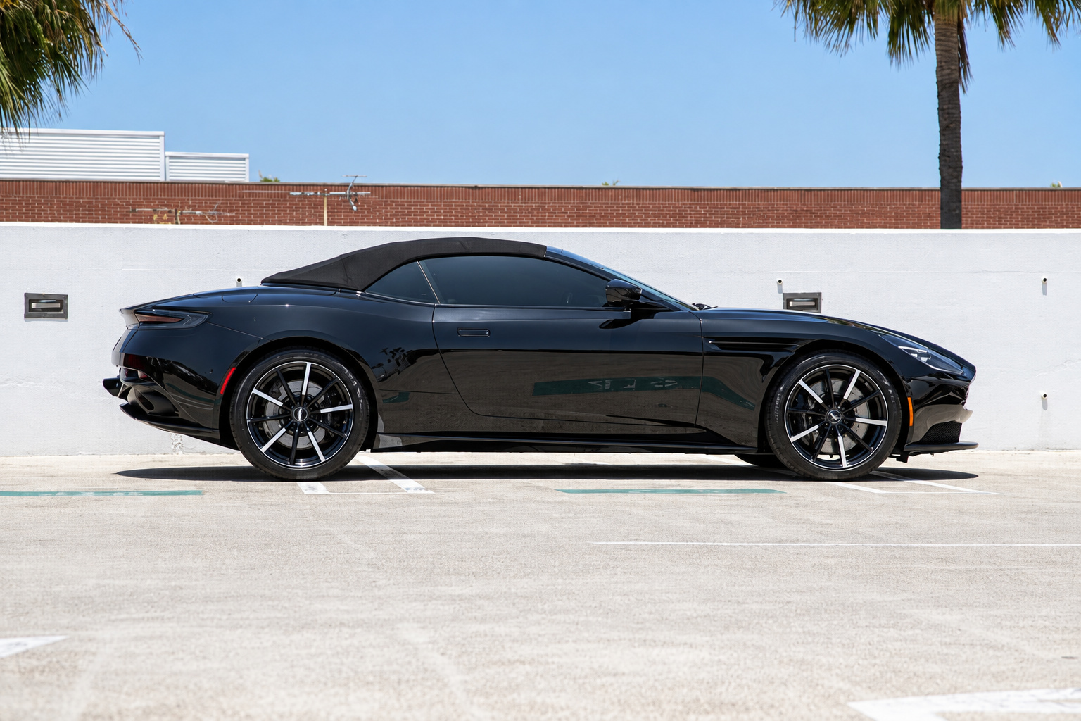 Side profile of the black Aston Martin DB11 Volante with the fabric roof closed, on black multi-spoke wheels