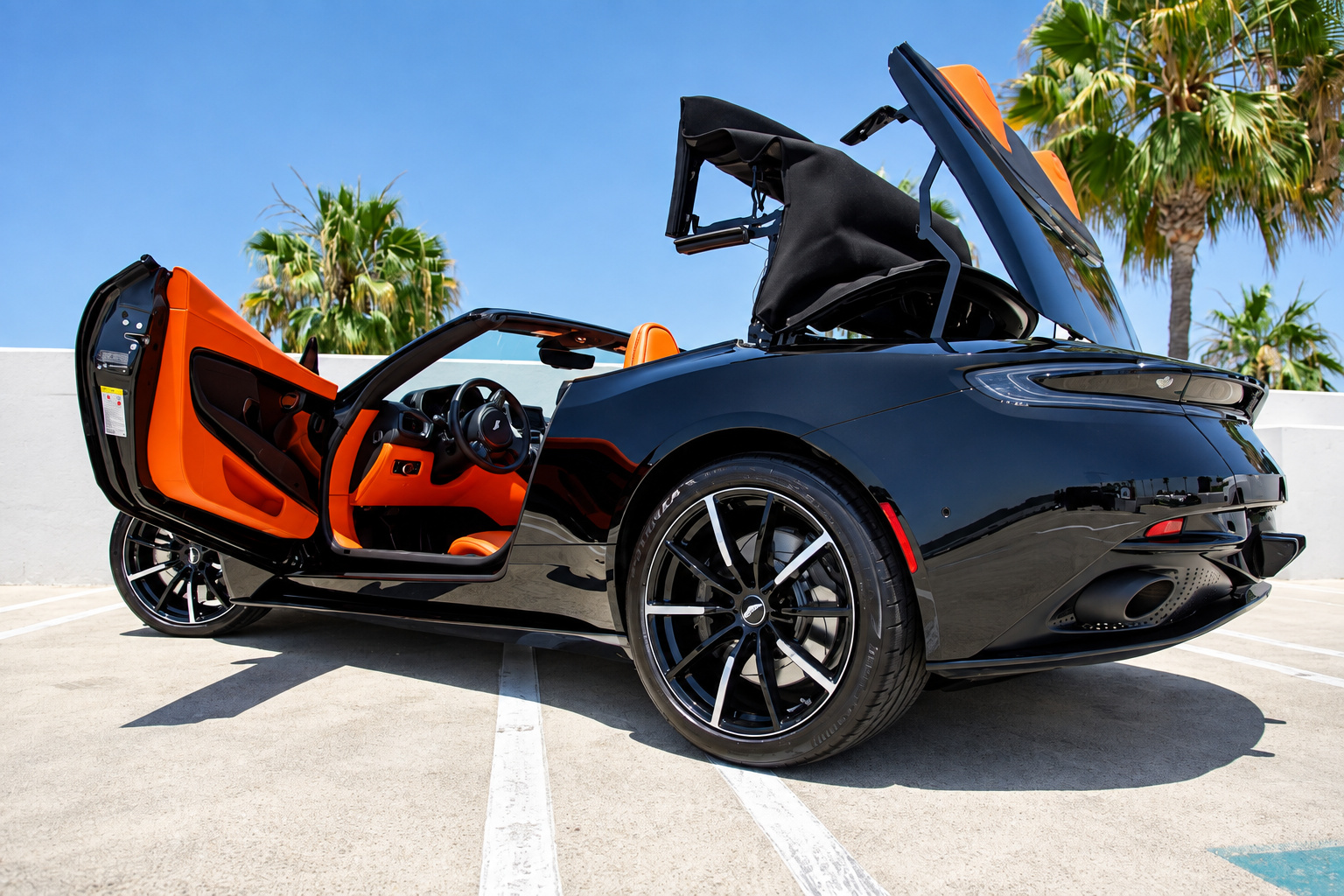Black Aston Martin DB11 Volante with both swan-wing doors open and the fabric roof mid-fold over the orange cabin