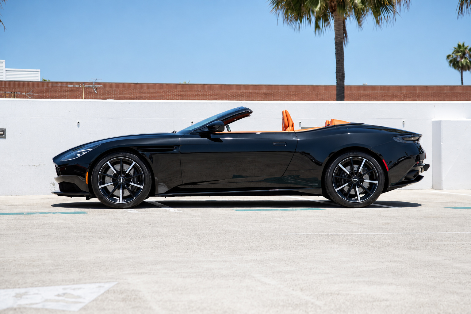 Side profile of the black Aston Martin DB11 Volante with the roof down, orange headrests above the black bodywork