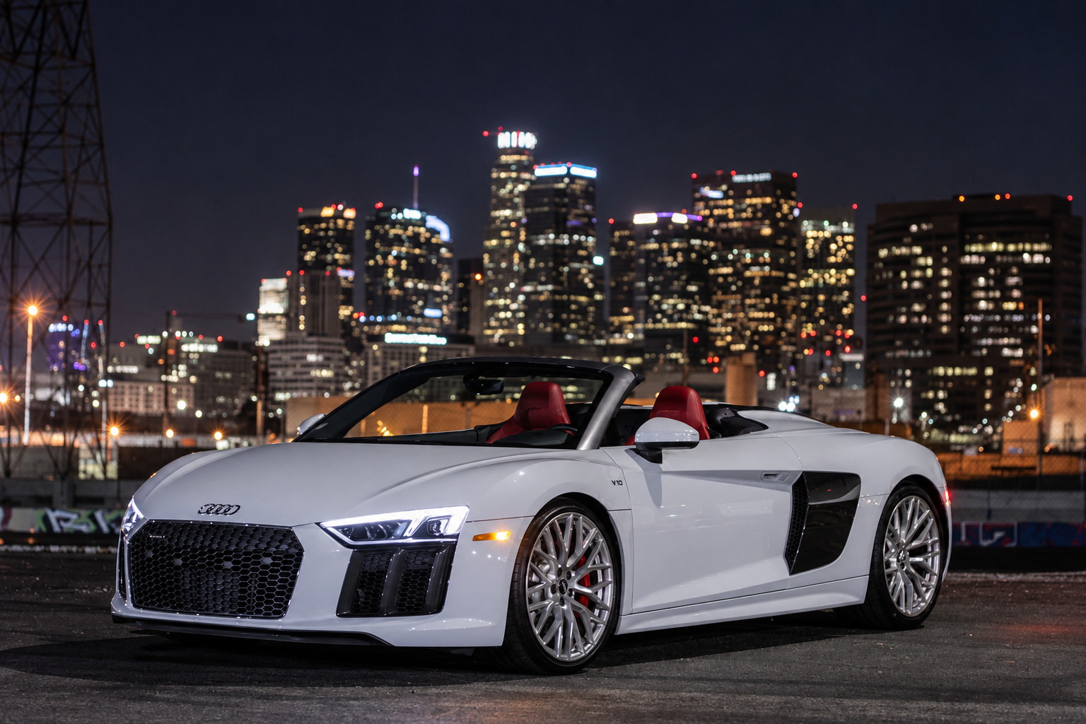 White Audi R8 V10 Spyder roof down at night with the downtown Los Angeles skyline lit up behind it