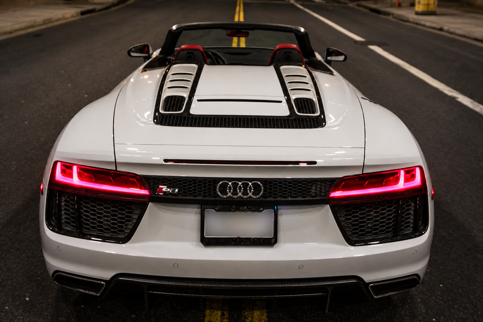Rear view of the white R8 V10 Spyder at night, roof down, red tail light bar and the vents over the V10