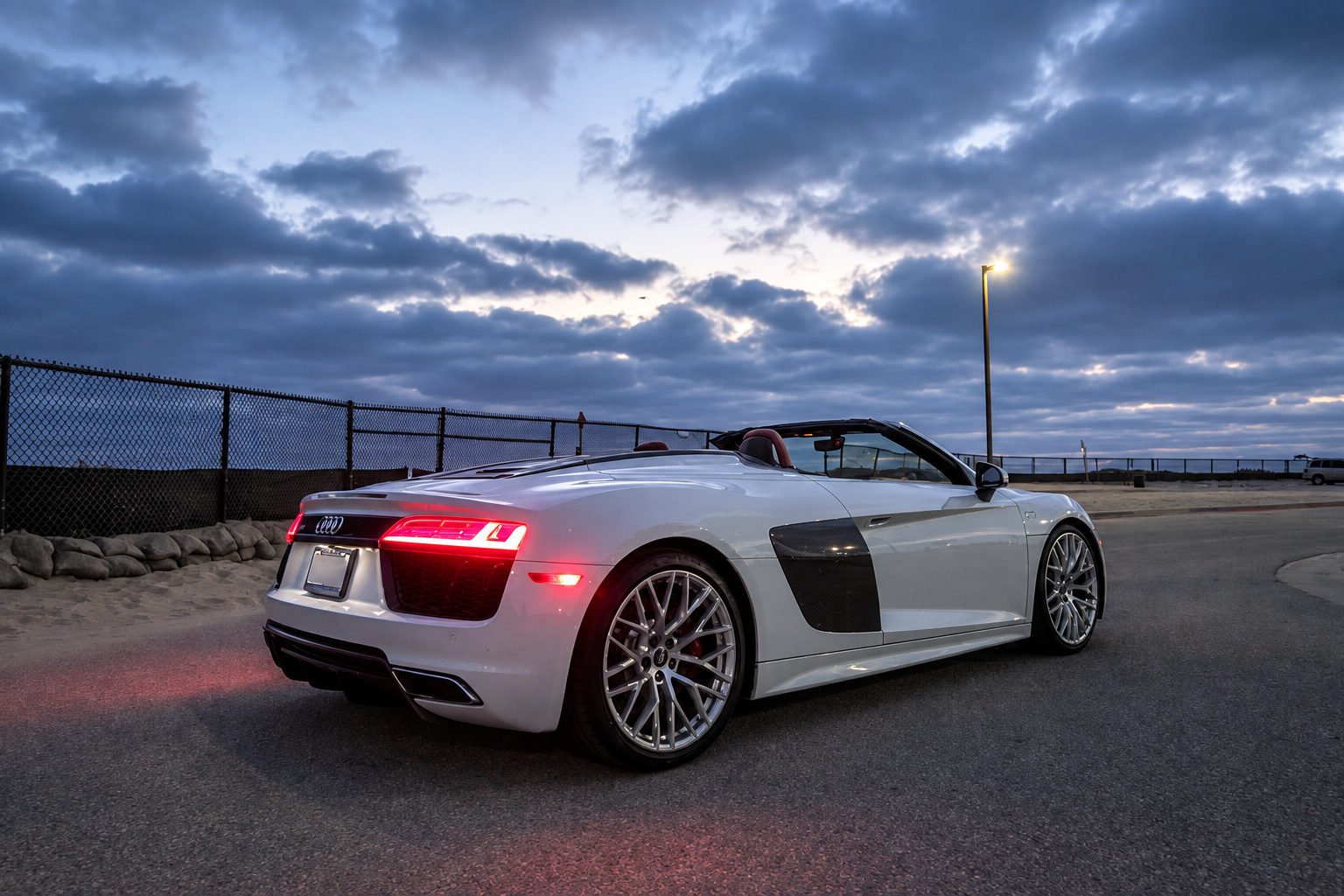 White Audi R8 Spyder from the rear three-quarter on a bluff at dusk with clouds over the coast