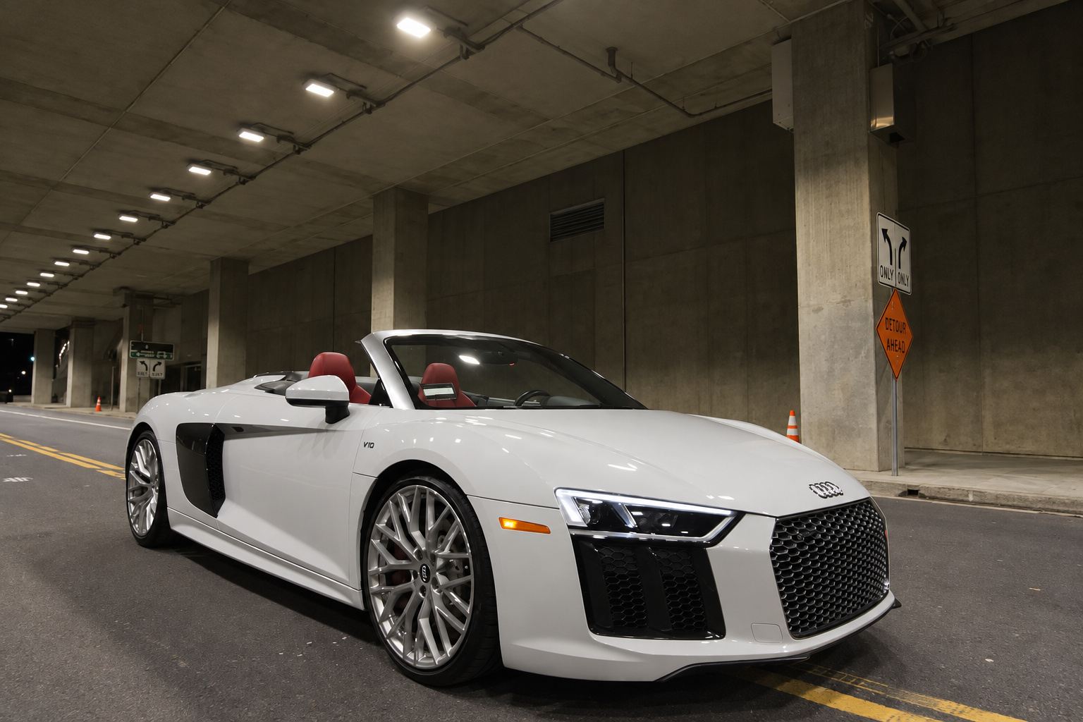 White R8 V10 Spyder parked roof down inside a concrete parking structure under the lights