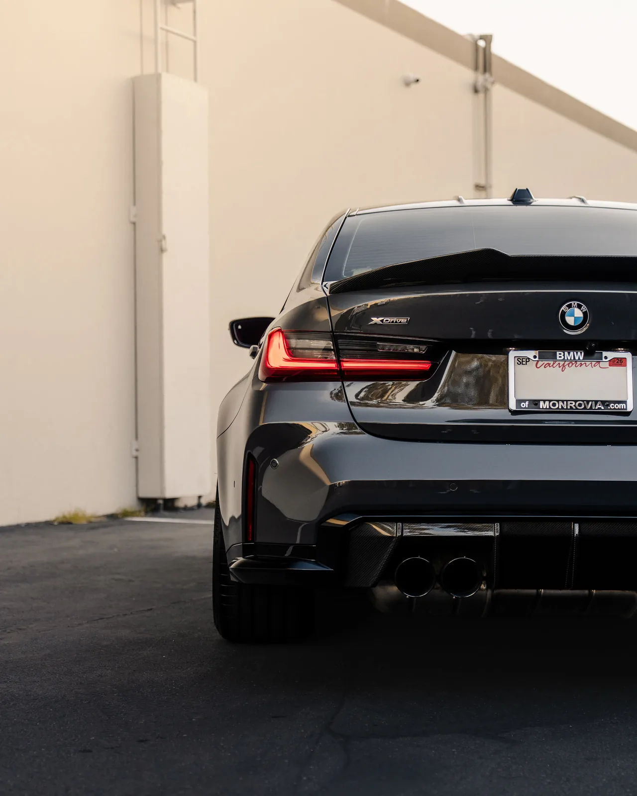 Rear view of the dark grey BMW M3 Competition, quad tailpipes and the rear diffuser under the tail lights