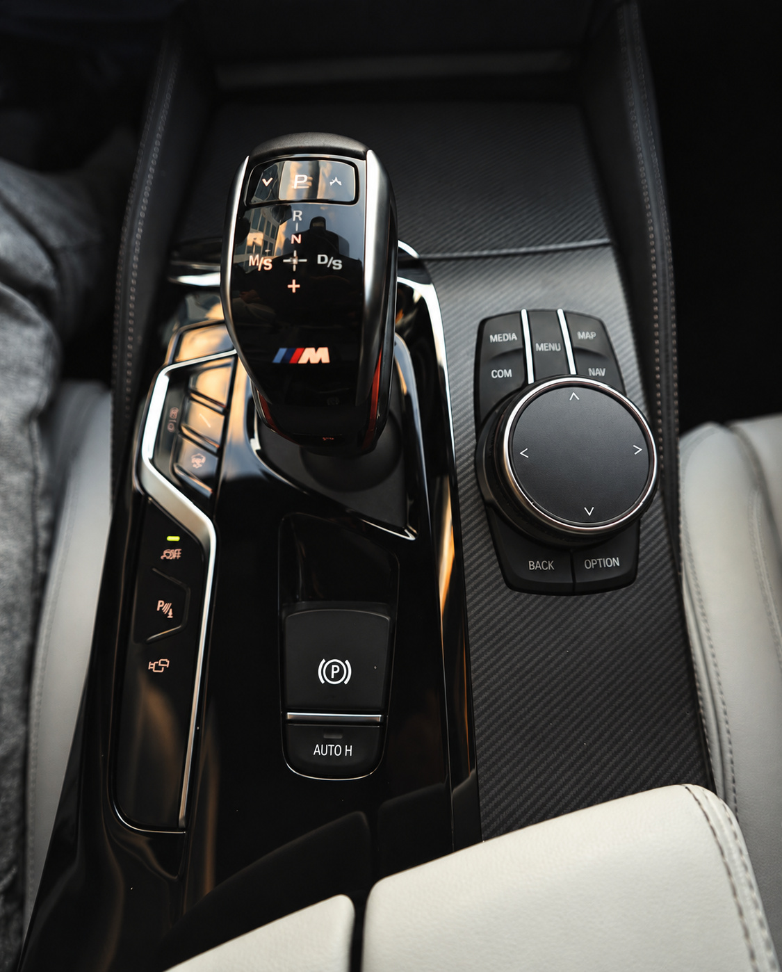 Close-up of the M5 Competition gear selector, iDrive controller and carbon fibre console trim