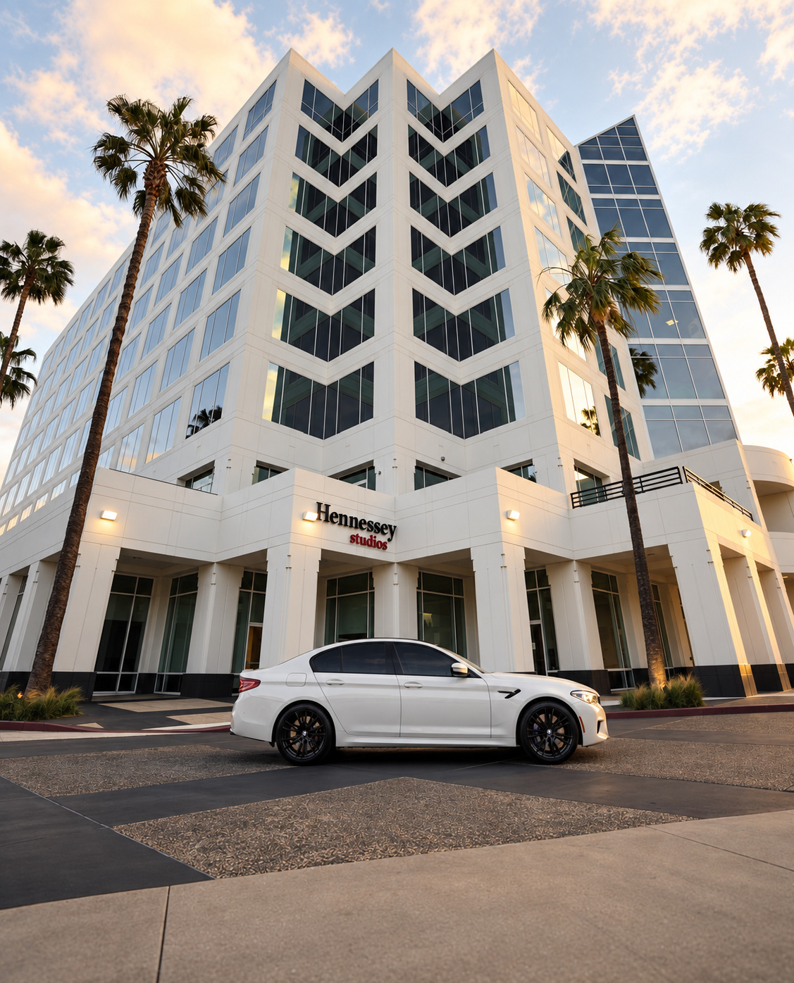 White BMW M5 Competition small in the frame below a tall office tower and a row of palm trees