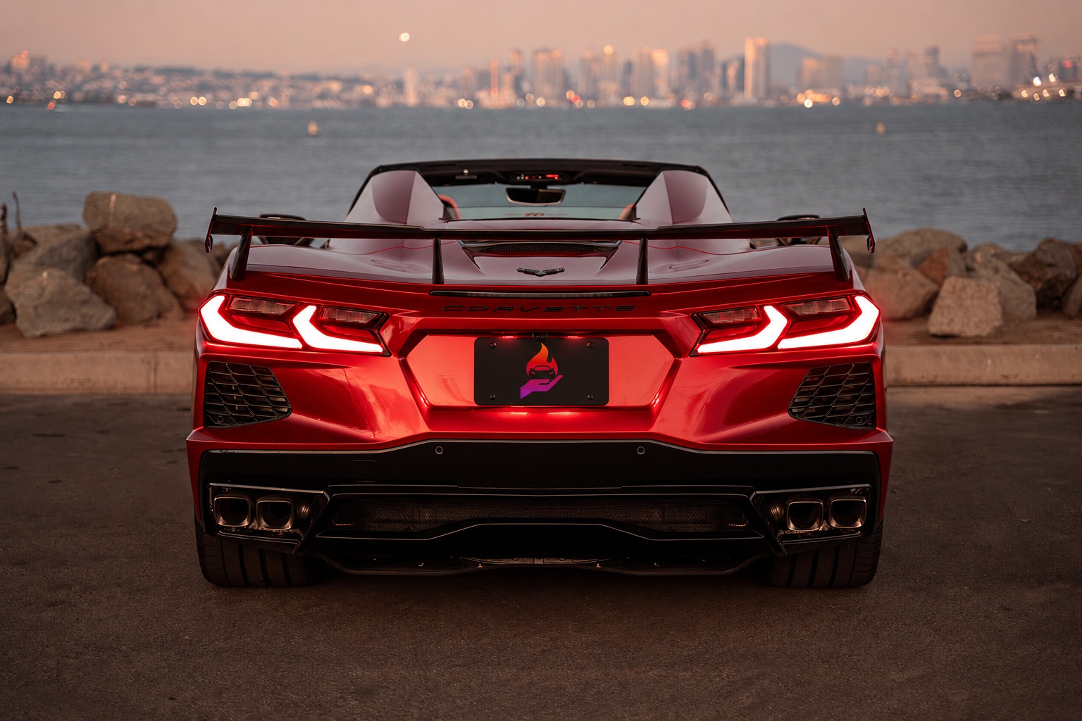 Rear view of the red C8 Stingray Convertible showing the high wing, quad exhaust and taillights, bay behind