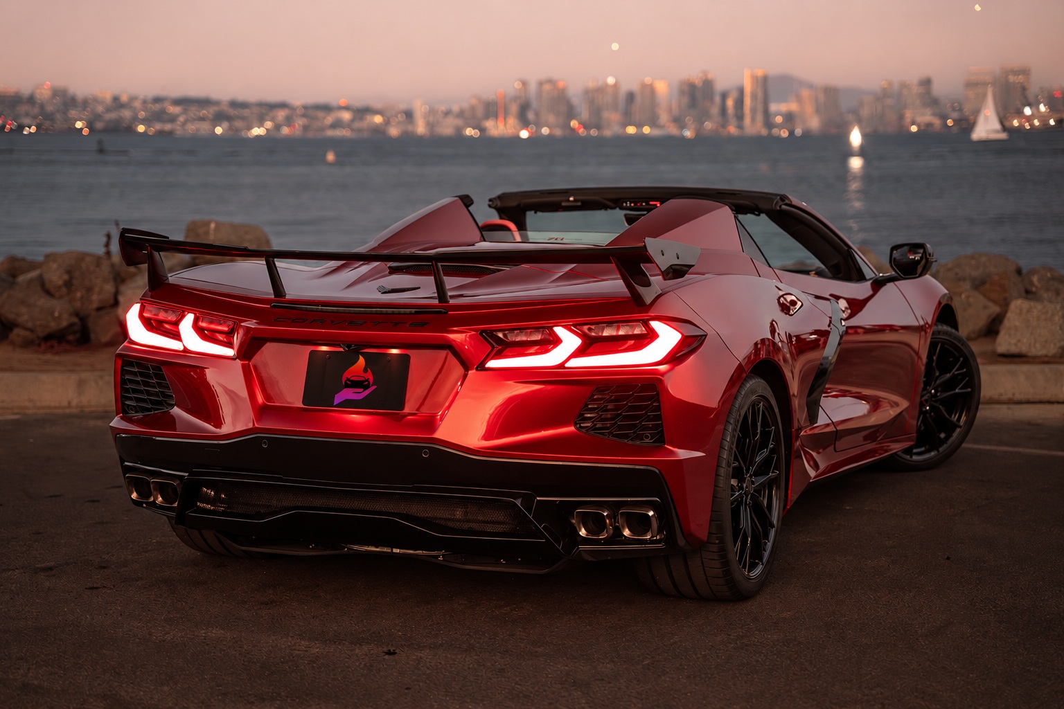 Rear three-quarter of the red Corvette C8 convertible on the bayfront at sunset, sailboat on the water