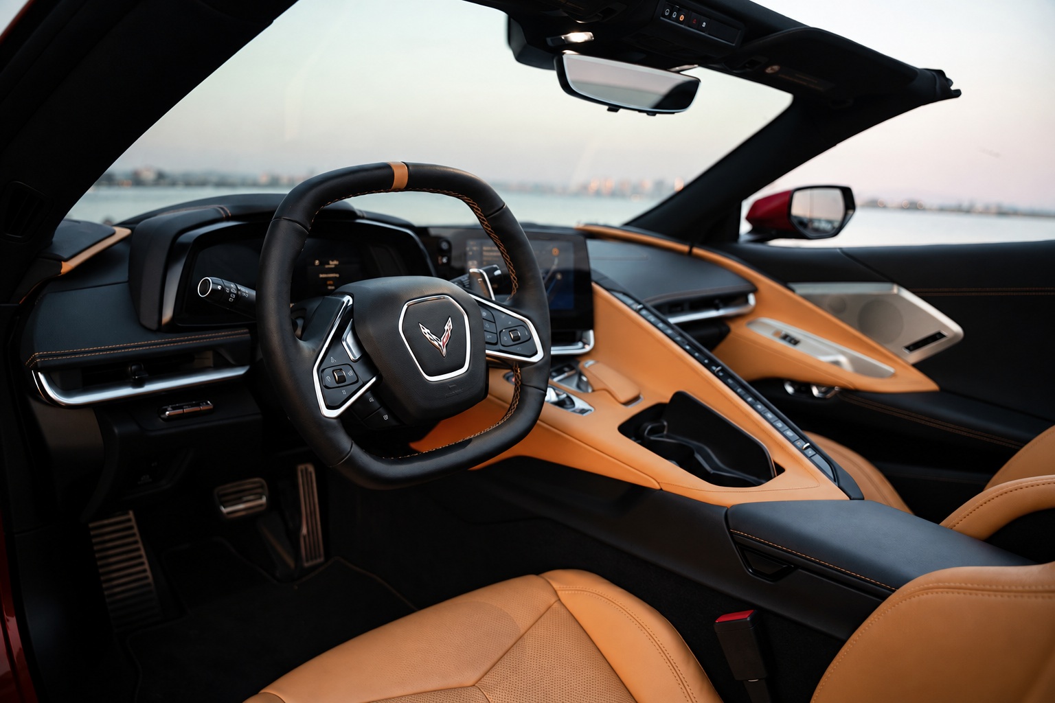 Driver's view of the tan Corvette C8 cabin, squared-off wheel, button wall and the bay through the windshield