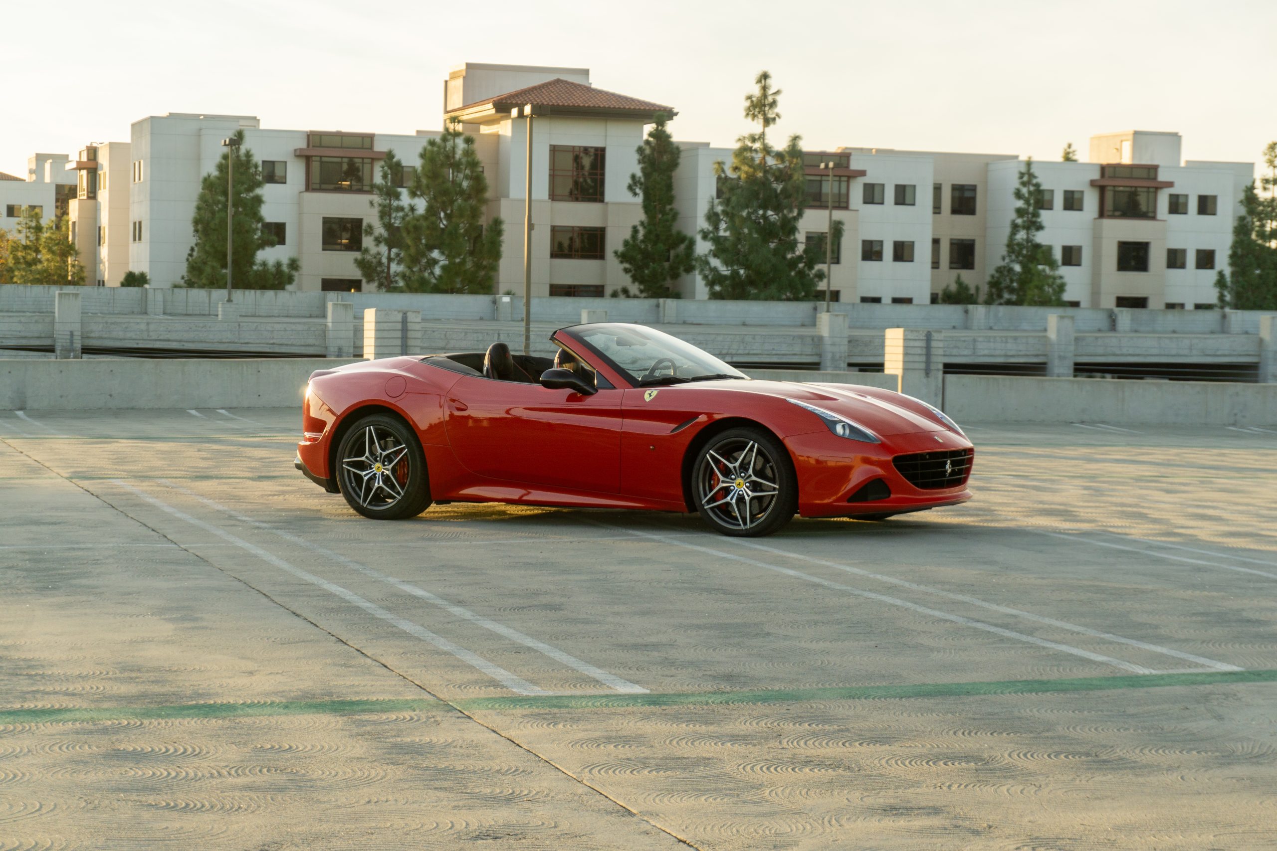 Red Ferrari California T, roof down, parked on a rooftop parking deck, front three-quarter view