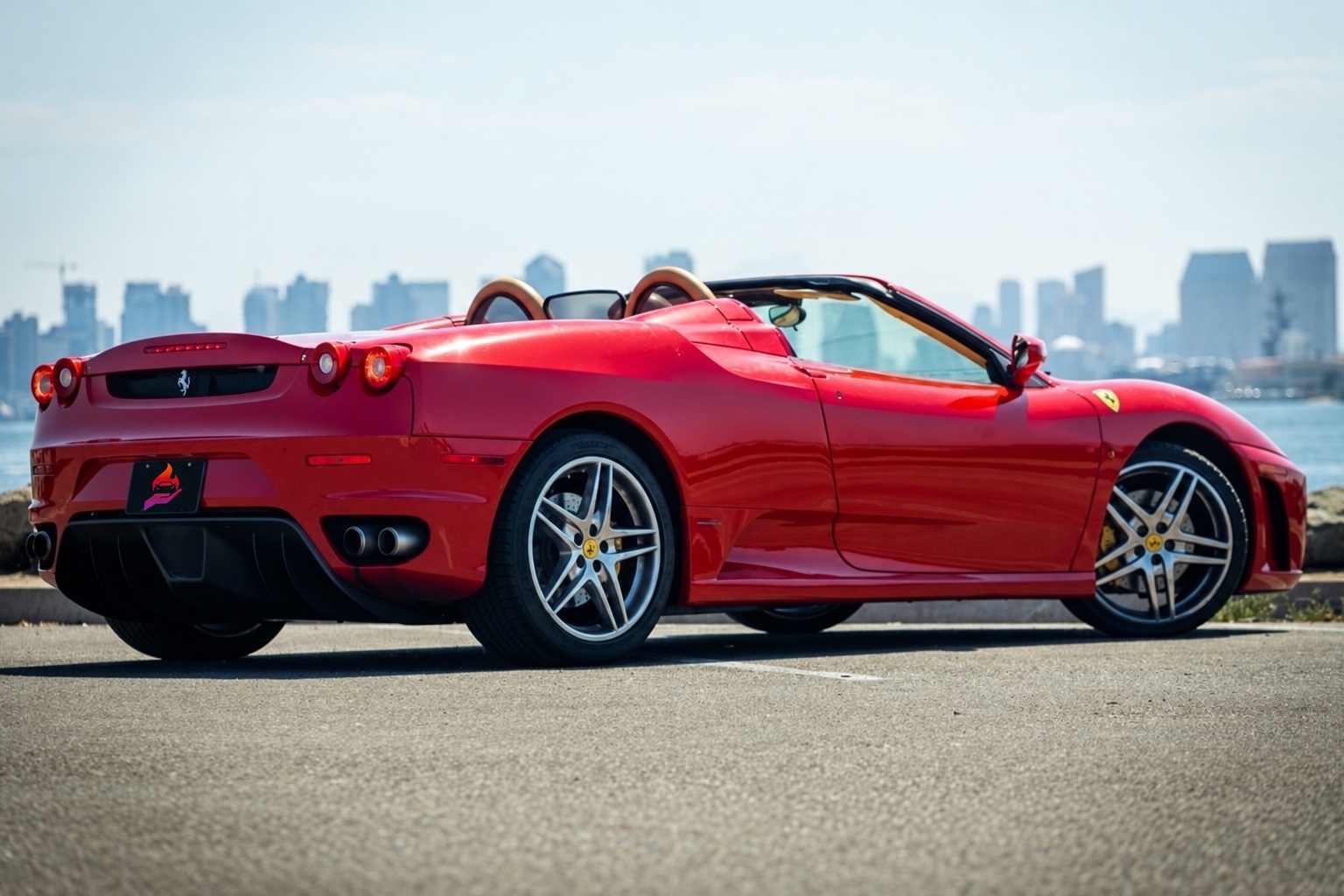 Rear three-quarter of the red Ferrari F430 Spider showing the roll hoops and silver star wheels, skyline across the water