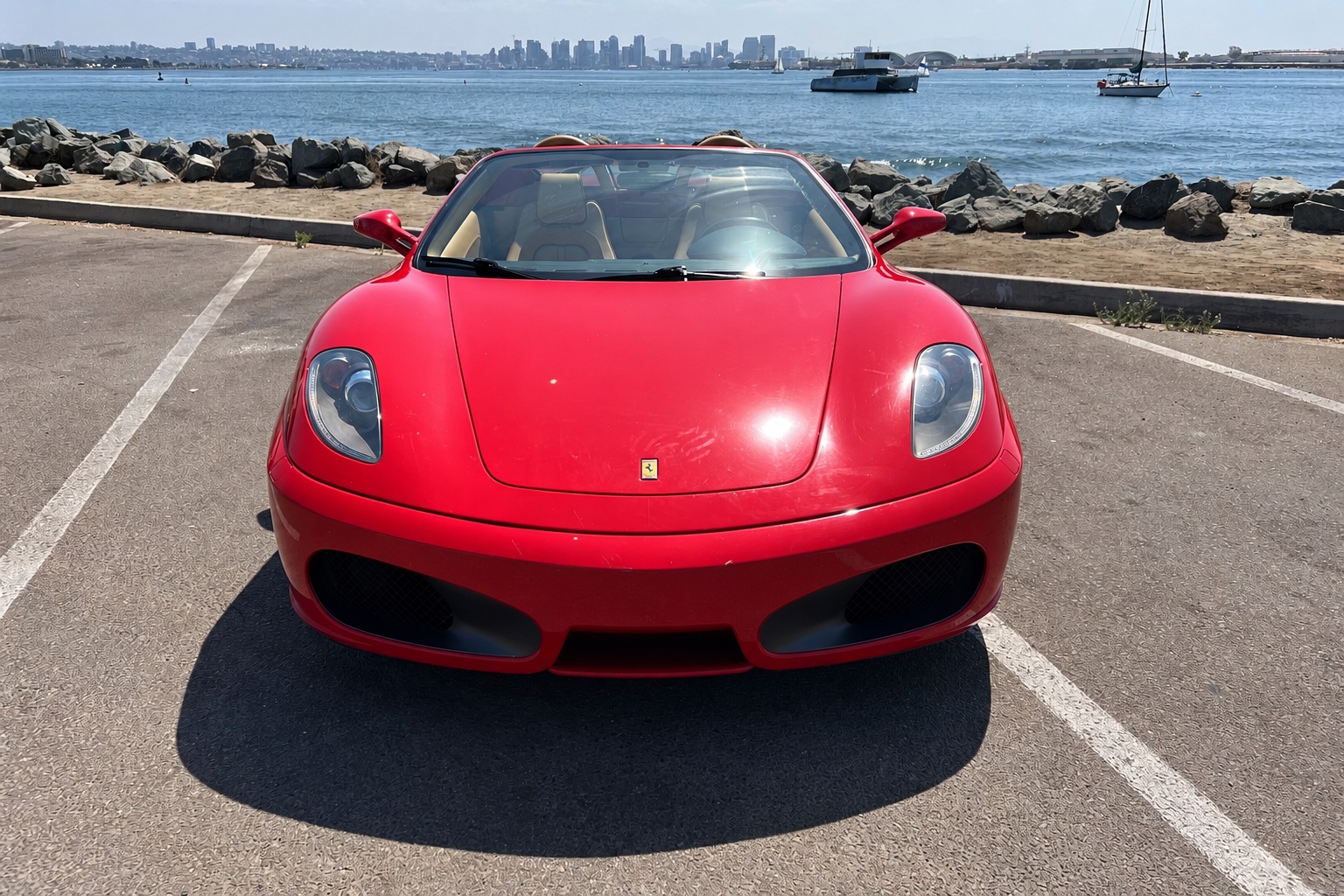 Head-on view of the red Ferrari F430 Spider with the roof down, open water and sailboats behind