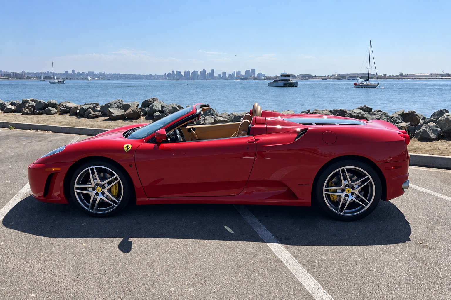 Side profile of the red Ferrari F430 Spider with the roof down, tan interior and sailboats behind