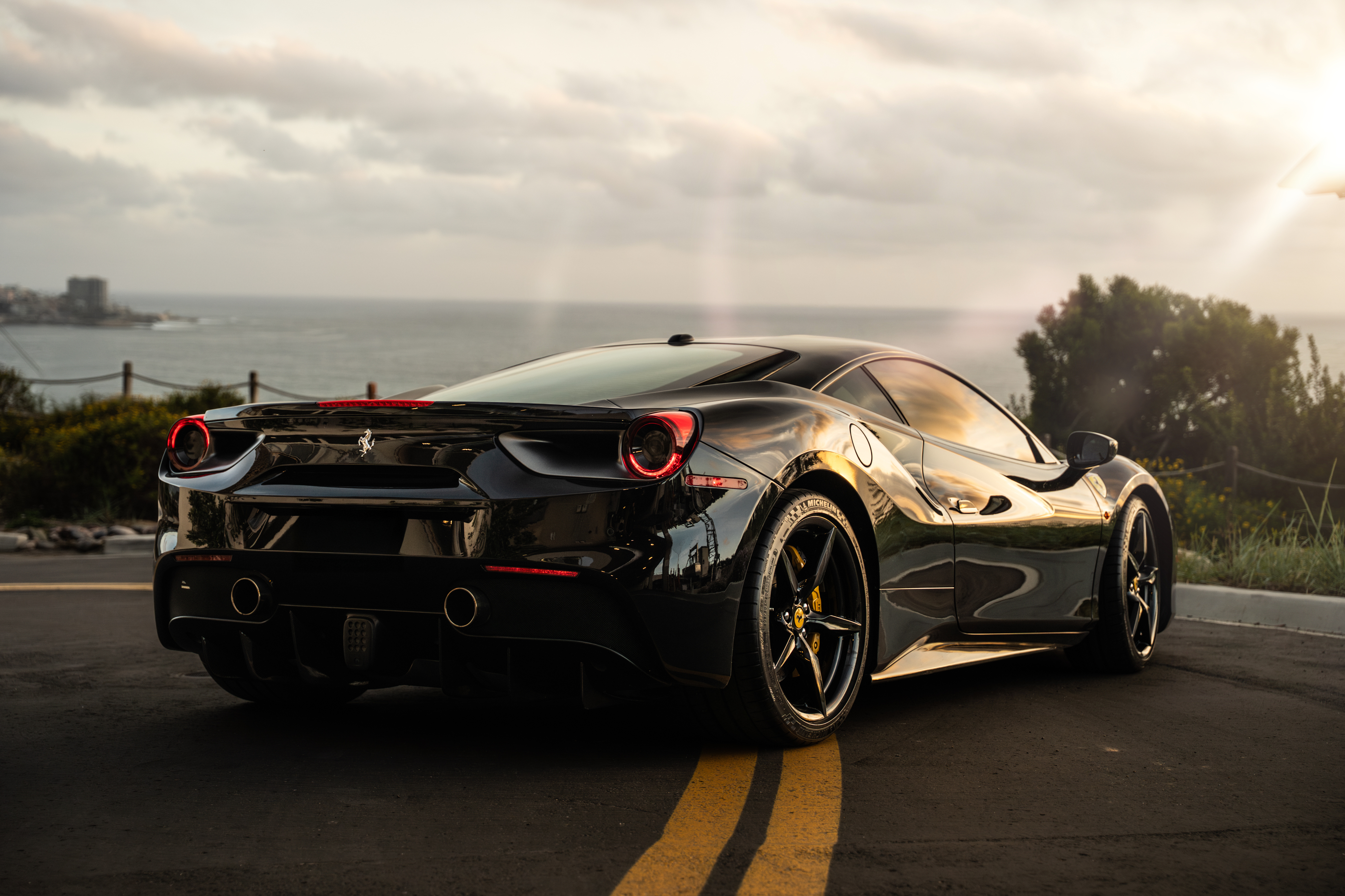 Rear three-quarter of the black 488 GTB on the coast road at sunset, black wheels and yellow calipers
