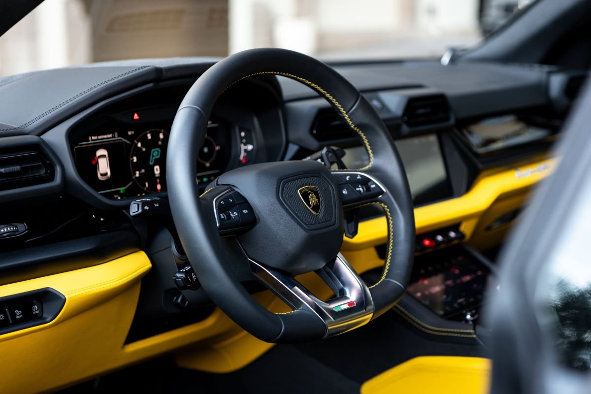 Steering wheel and driver's screen in the Urus SE with the yellow leather door top beside it