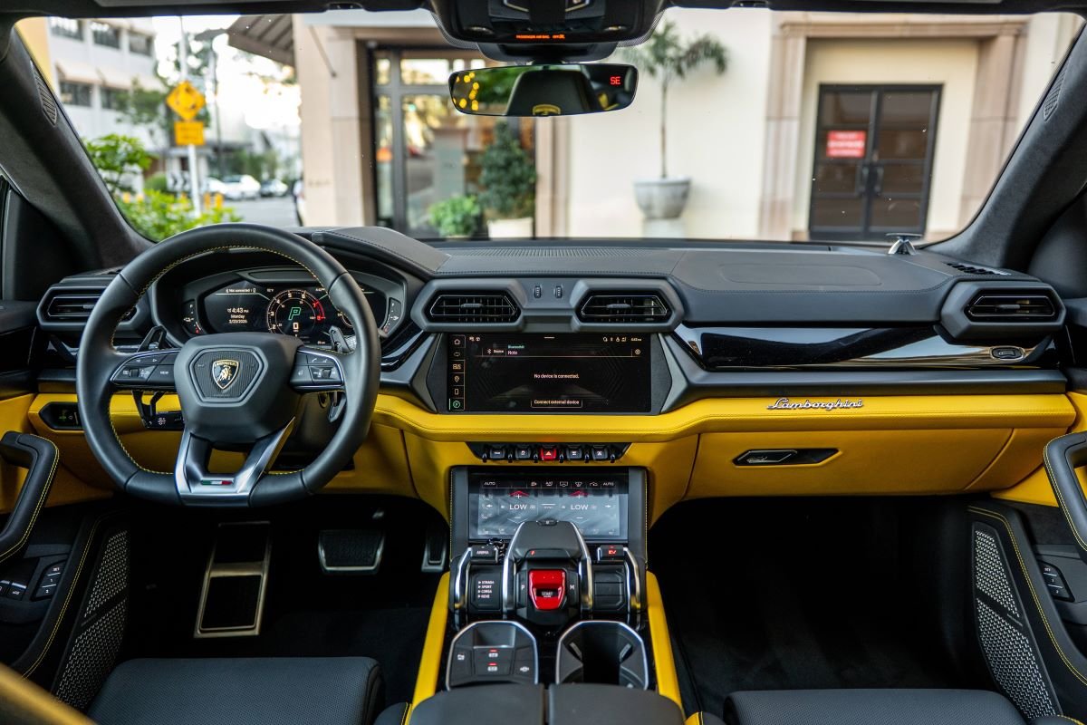 Full dash of the Lamborghini Urus SE from the back seat, yellow door tops, yellow console sides and twin screens