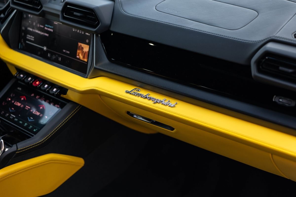Passenger side of the Urus SE dash with the yellow leather strip, Lamborghini script and the lower screen