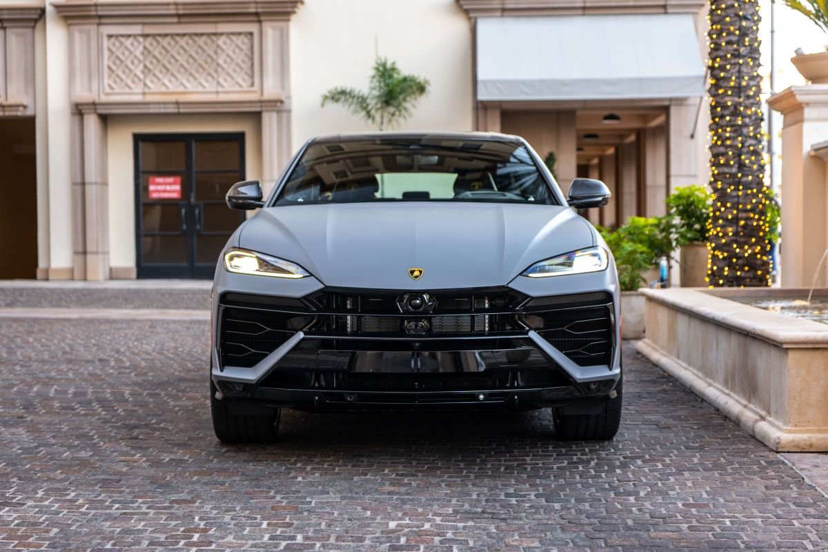 Head-on view of the grey Lamborghini Urus SE in a courtyard with a fountain and palm trees