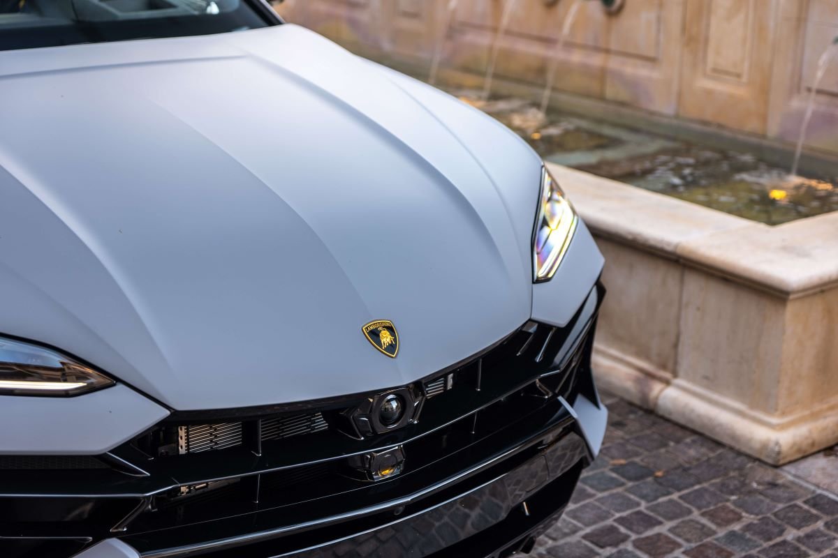 Hood and headlight of the grey Urus SE from above with a stone fountain wall behind