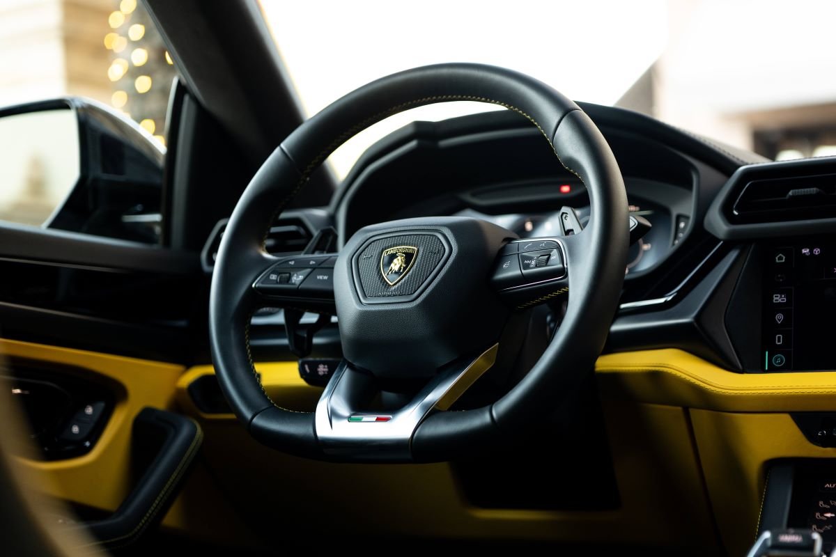 Close view of the Urus SE steering wheel with the Italian flag tab and the yellow door leather behind