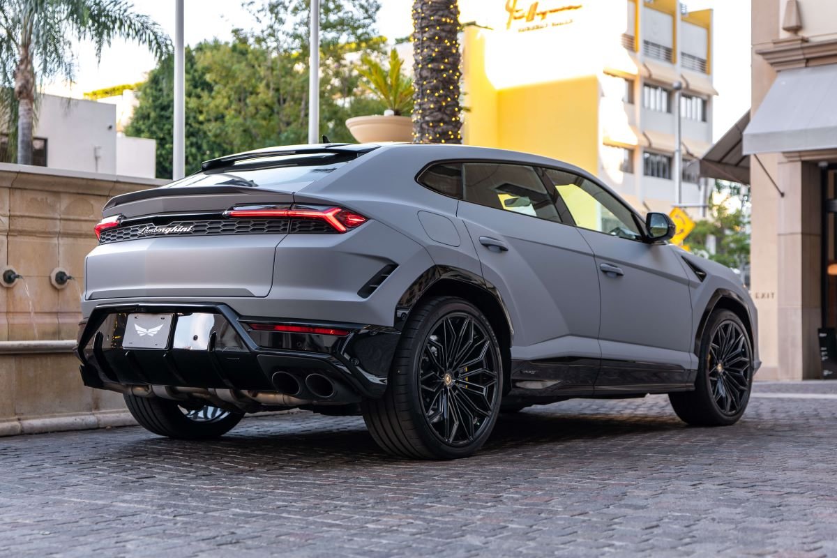 Rear three-quarter of the grey Urus SE on cobbles, roof spoiler, quad exhausts and black wheels