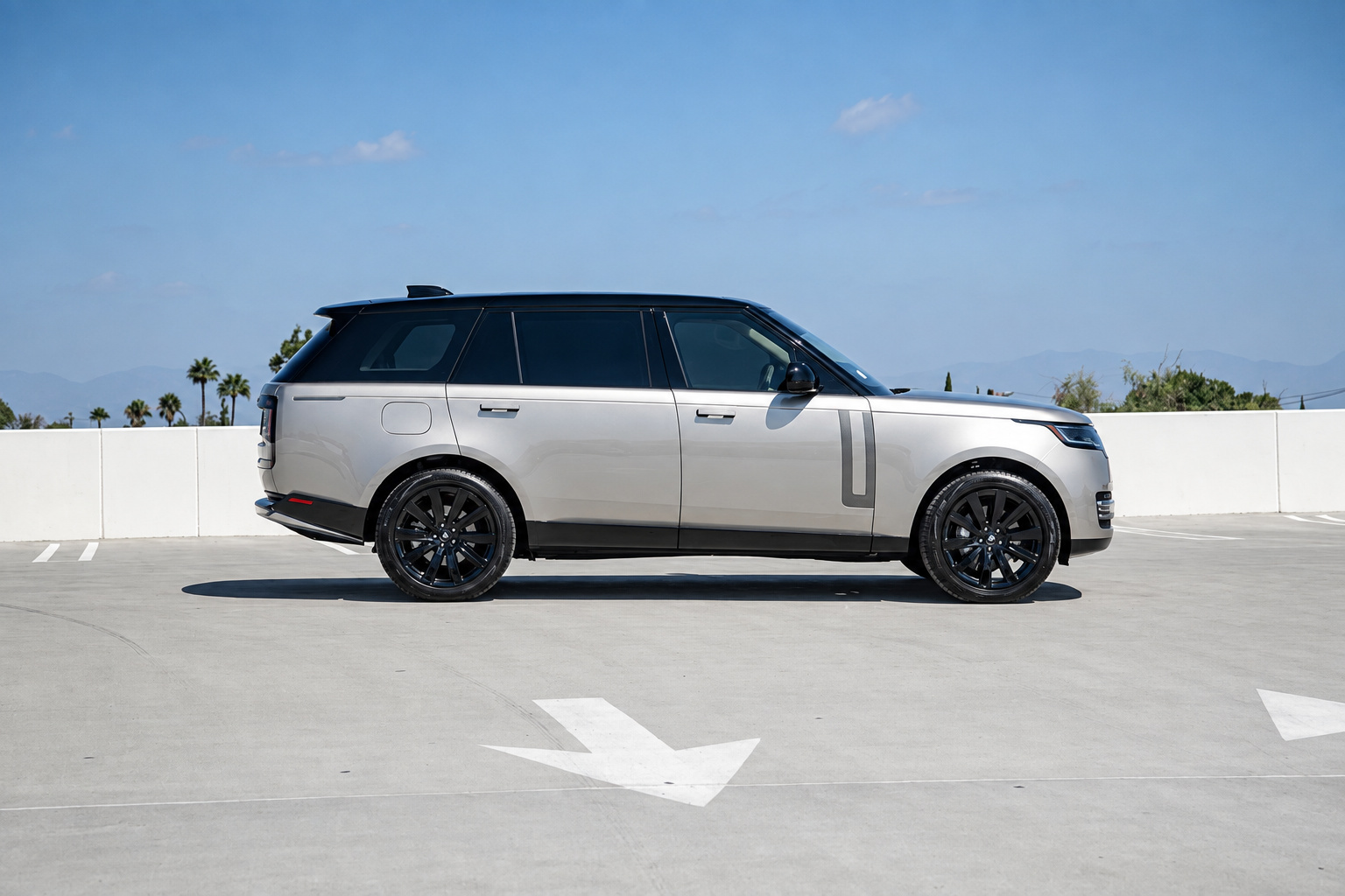 Side profile of the champagne Range Rover HSE on a rooftop parking deck with mountains in the distance