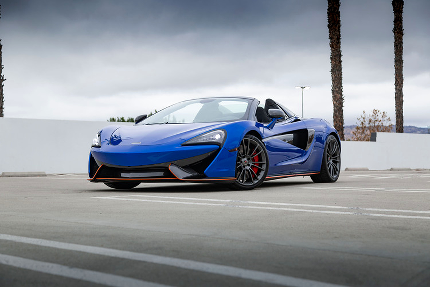 Vega Blue McLaren 570S Spider with the roof down, front three-quarter on a rooftop deck with palm trees