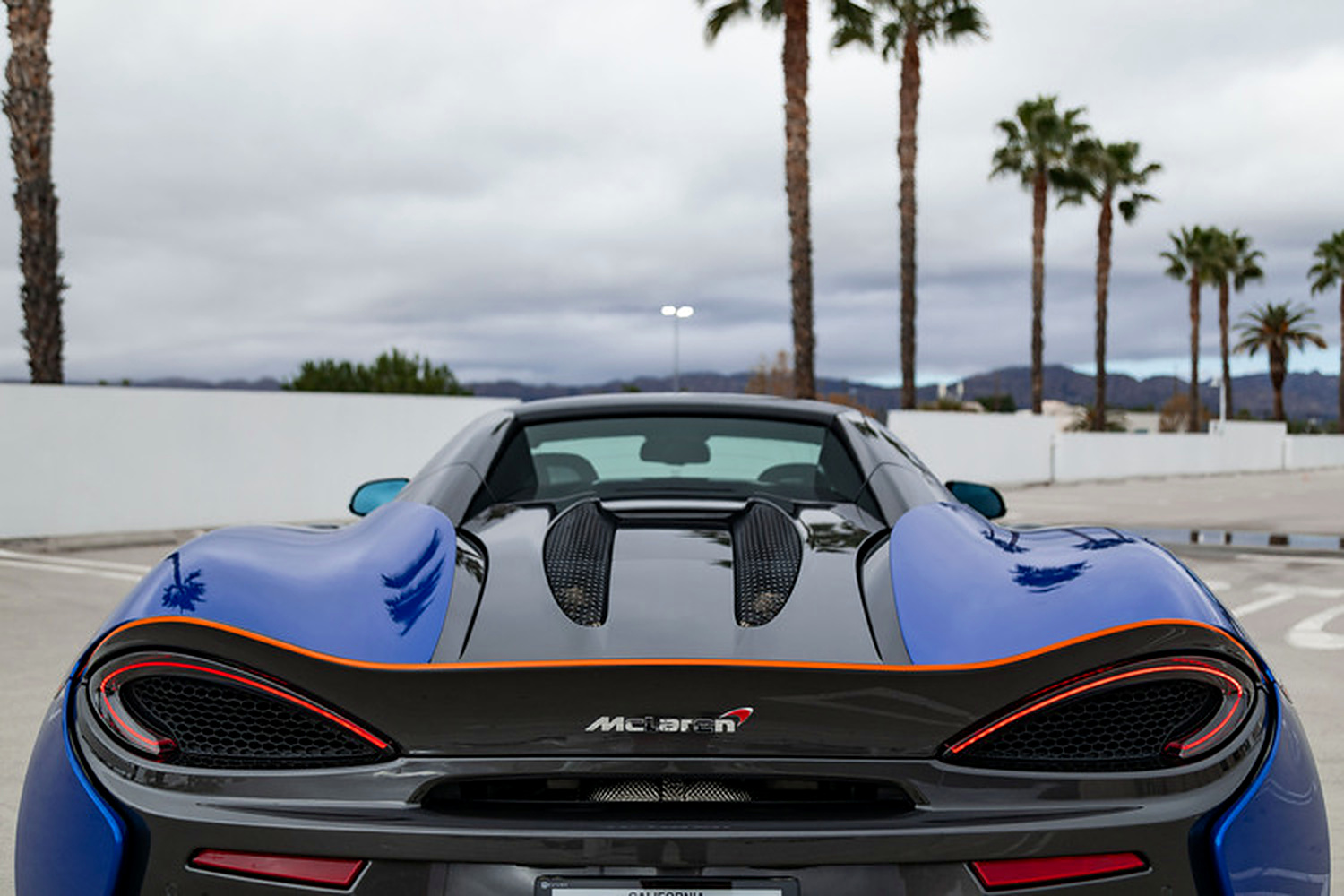 Rear view of the McLaren 570S Spider with the roof down, orange pinstripe on the wing lip and diffuser