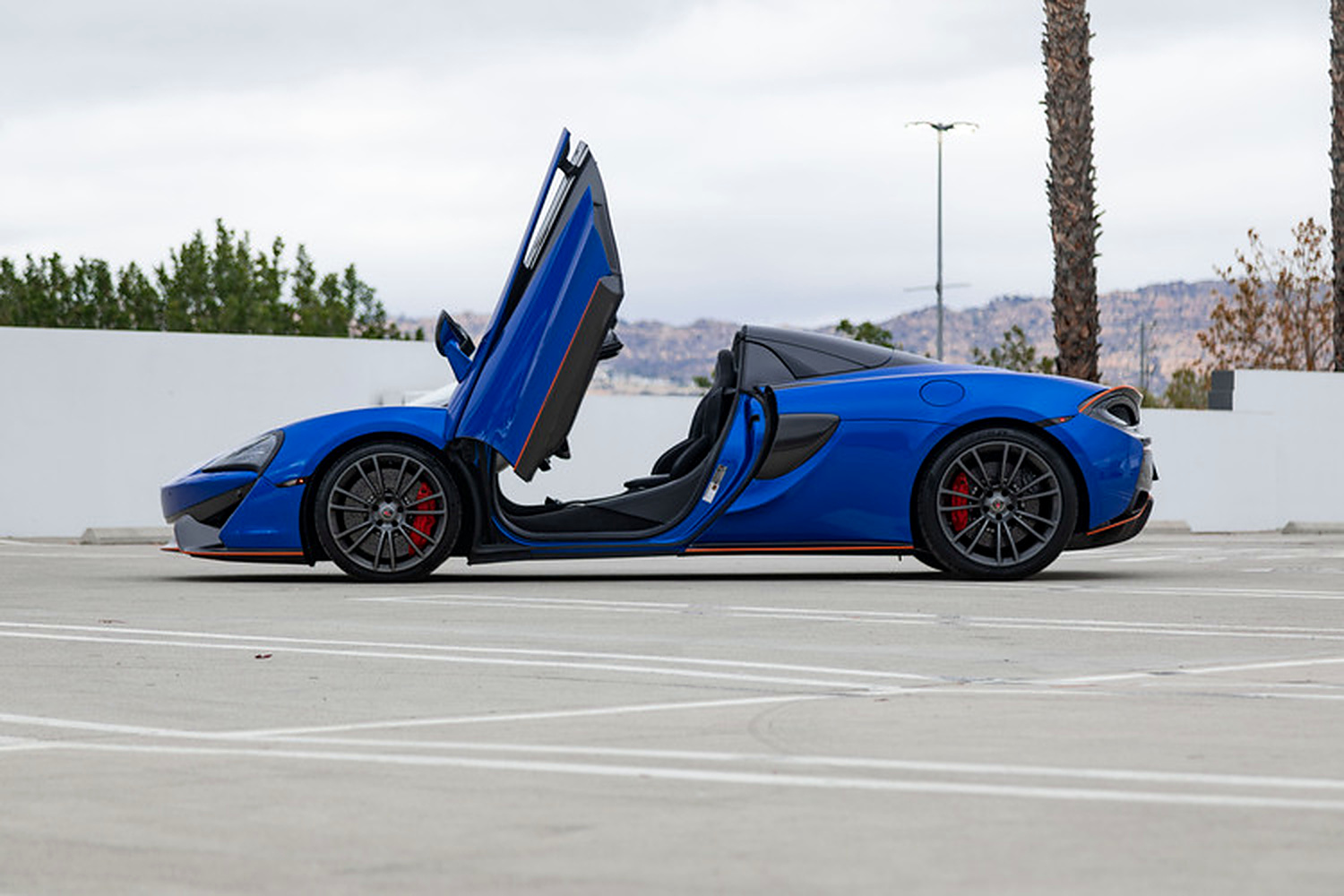 Side profile of the blue 570S Spider with both doors up and the roof down, mountains in the distance