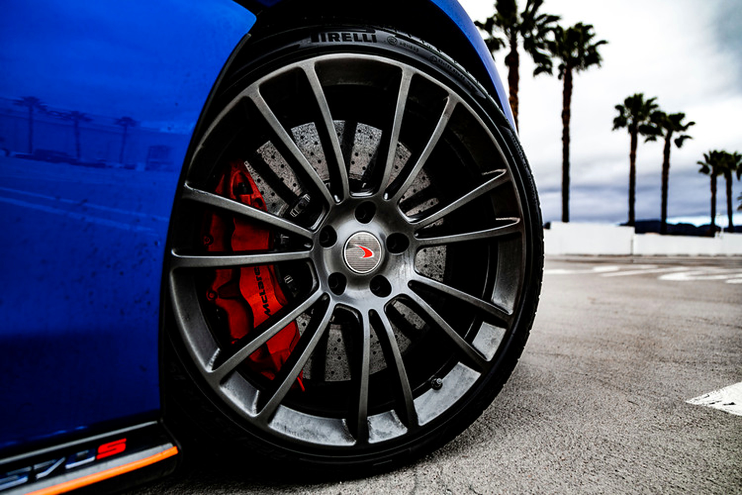 Dark multi-spoke wheel of the McLaren 570S Spider with the red caliper and the orange sill stripe